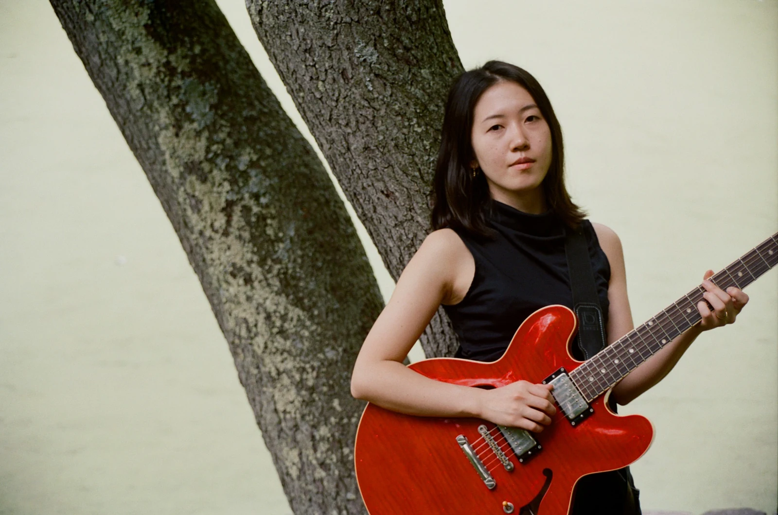 Erika Toda with her red electric guitar beside a tree